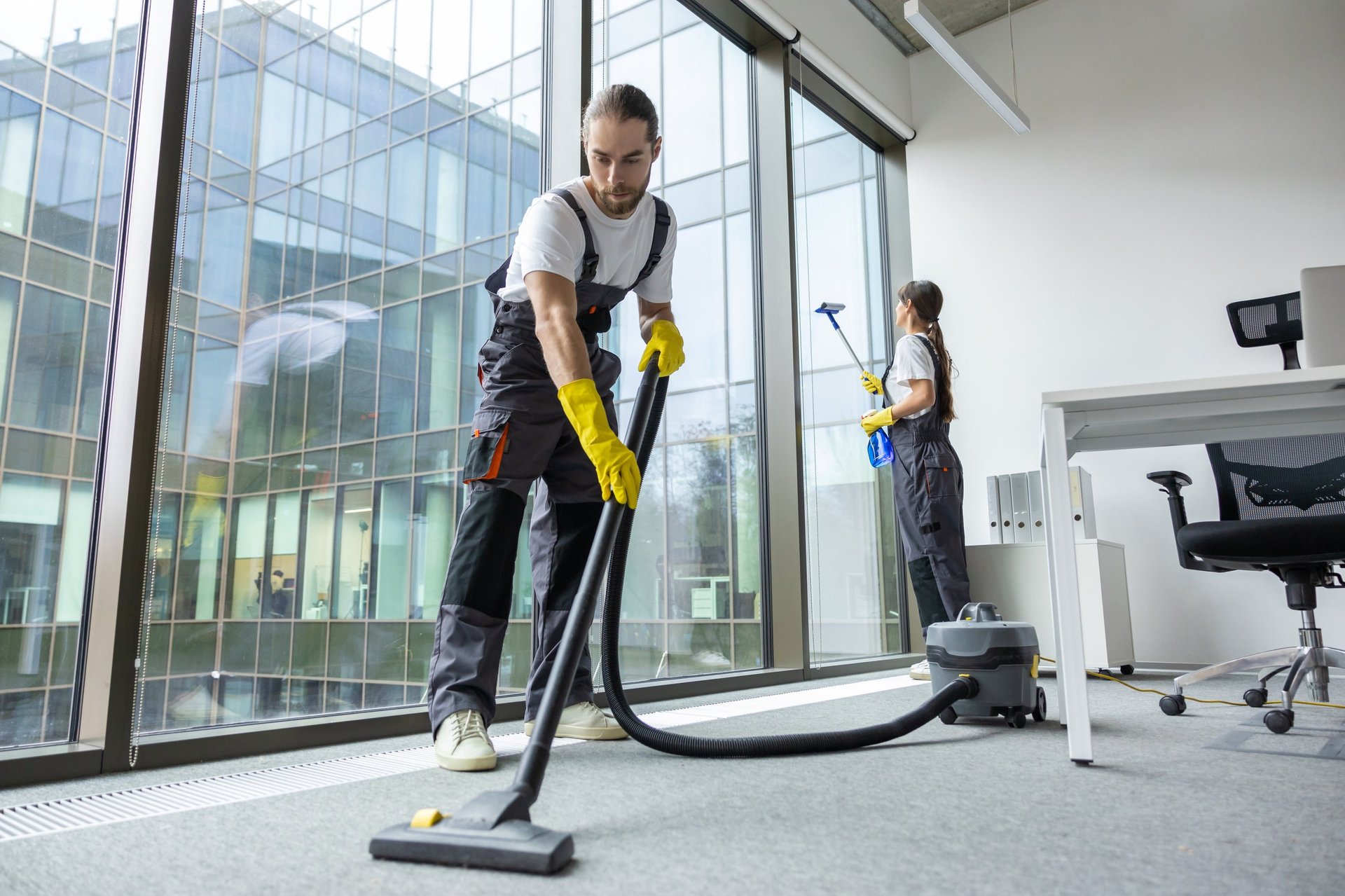 Vacuum cleaning. Young man in uniform vacuum cleaning the floor in the conference room